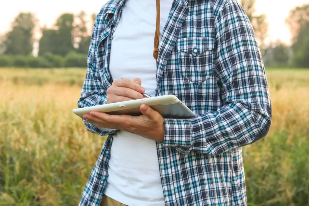 Farmer in the field, using a tablet app to aid in agricultural tasks. Close-up of hands.